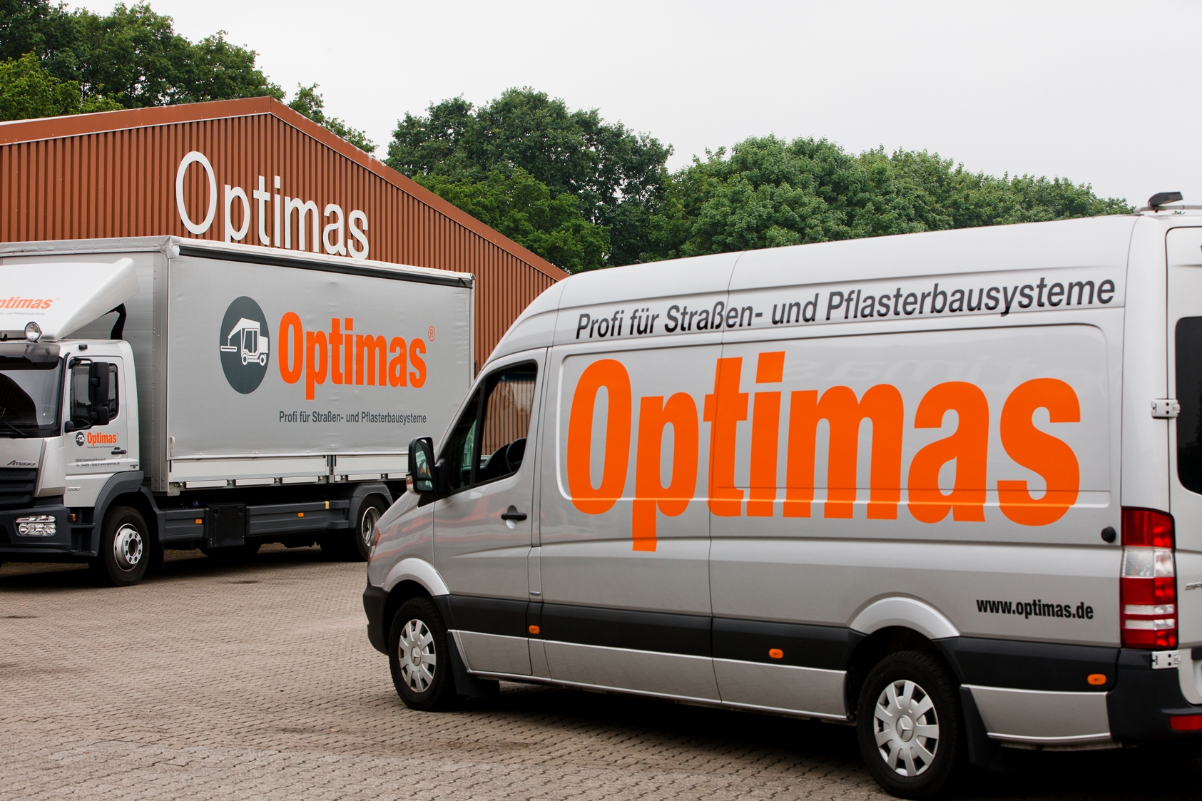 Two vehicles branded with the Optimas logo parked outside a building with the same branding – Optimas.