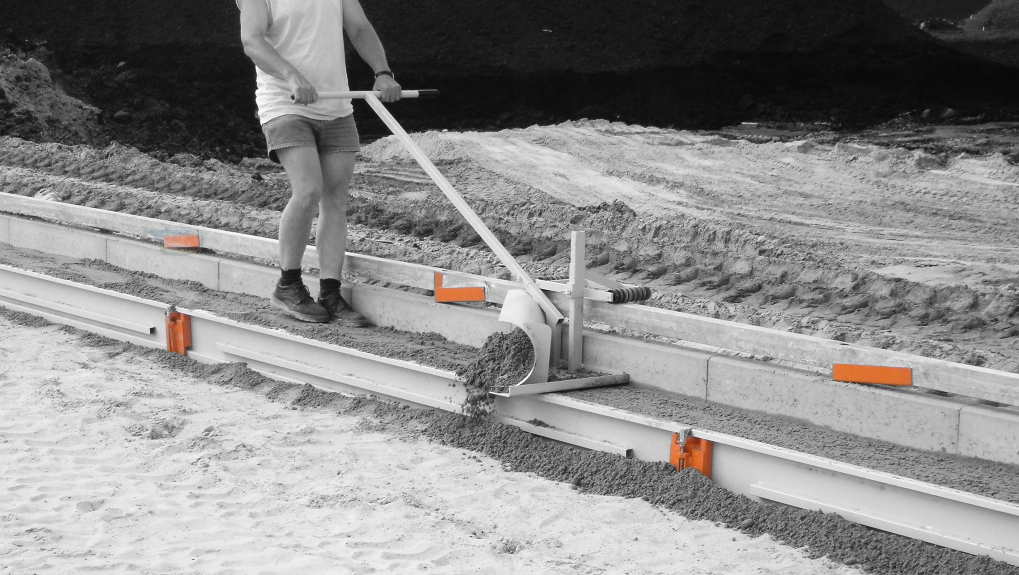 A worker using a concrete screed machine to level wet concrete on a construction site – Optimas.