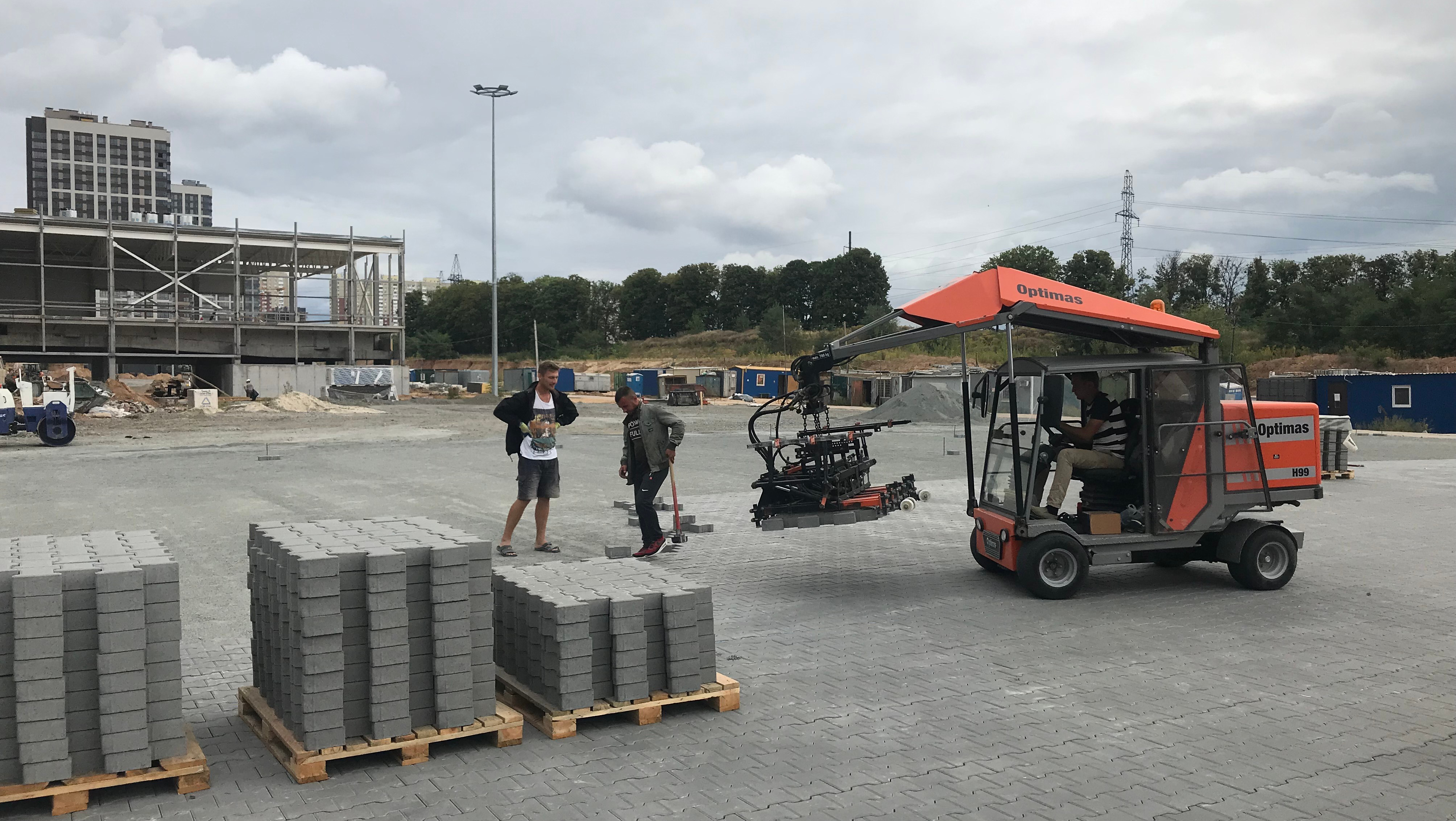 Construction site with workers and a machine lifting concrete blocks, showcasing efficient material handling – Optimas.