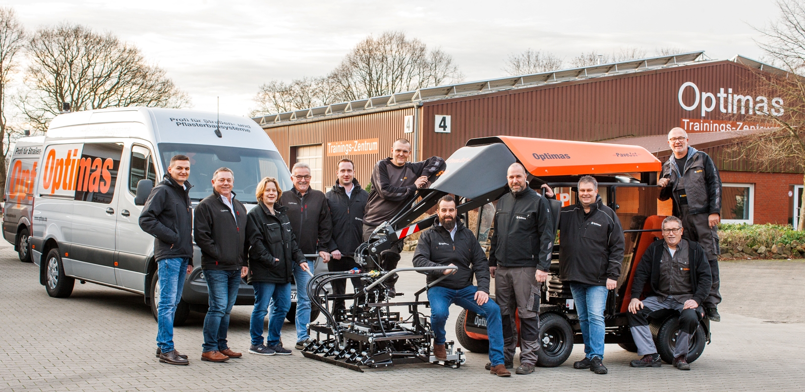 A group of professionals in front of an Optimas training center and vehicle, showcasing teamwork and innovation – Optimas.