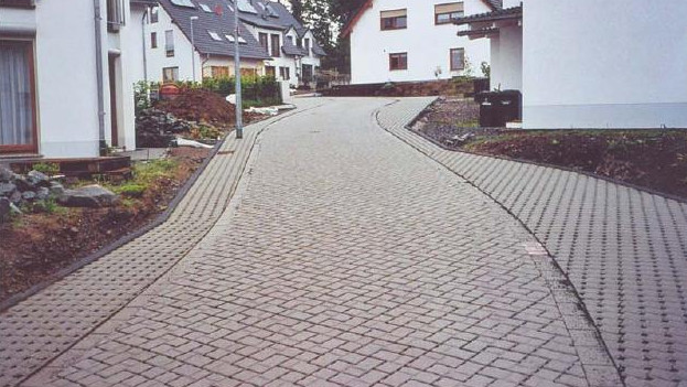 A paved road winding through a residential area with houses on either side – Optimas.