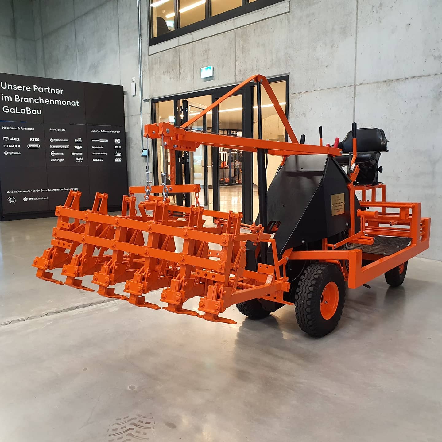 Bright orange, heavy-duty industrial machine on display indoors, showcasing its complex design. – Optimas