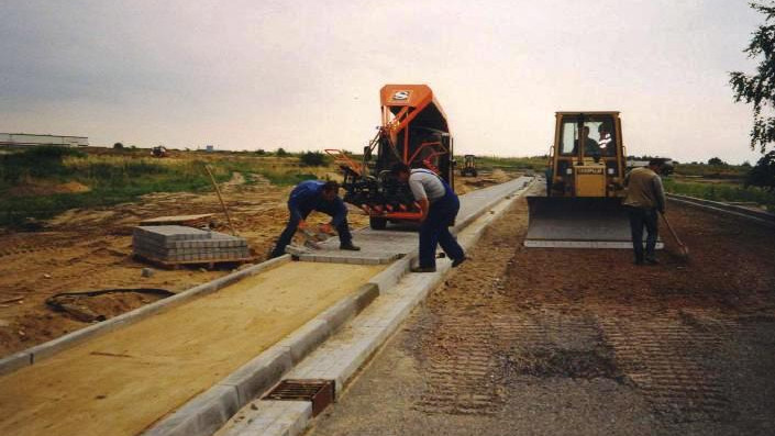 Construction workers laying concrete for a sidewalk with machinery and tools on a construction site – Optimas.
