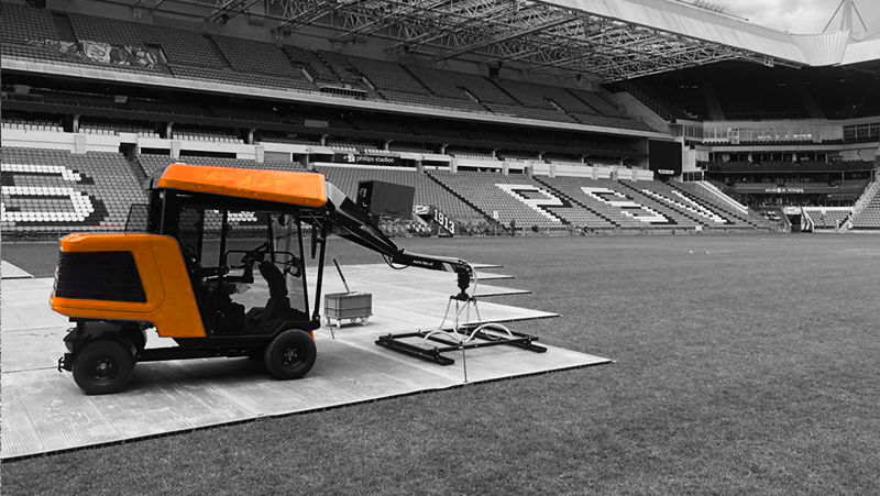 Orange turf management vehicle utilizing light technology stands on a sports field inside of a stadium to maintain the grass quality – Optimas