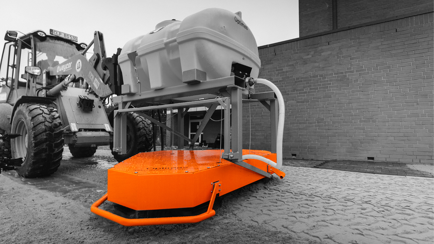 An orange industrial machine with a tank, positioned next to a tractor on a cobblestone surface – Optimas.
