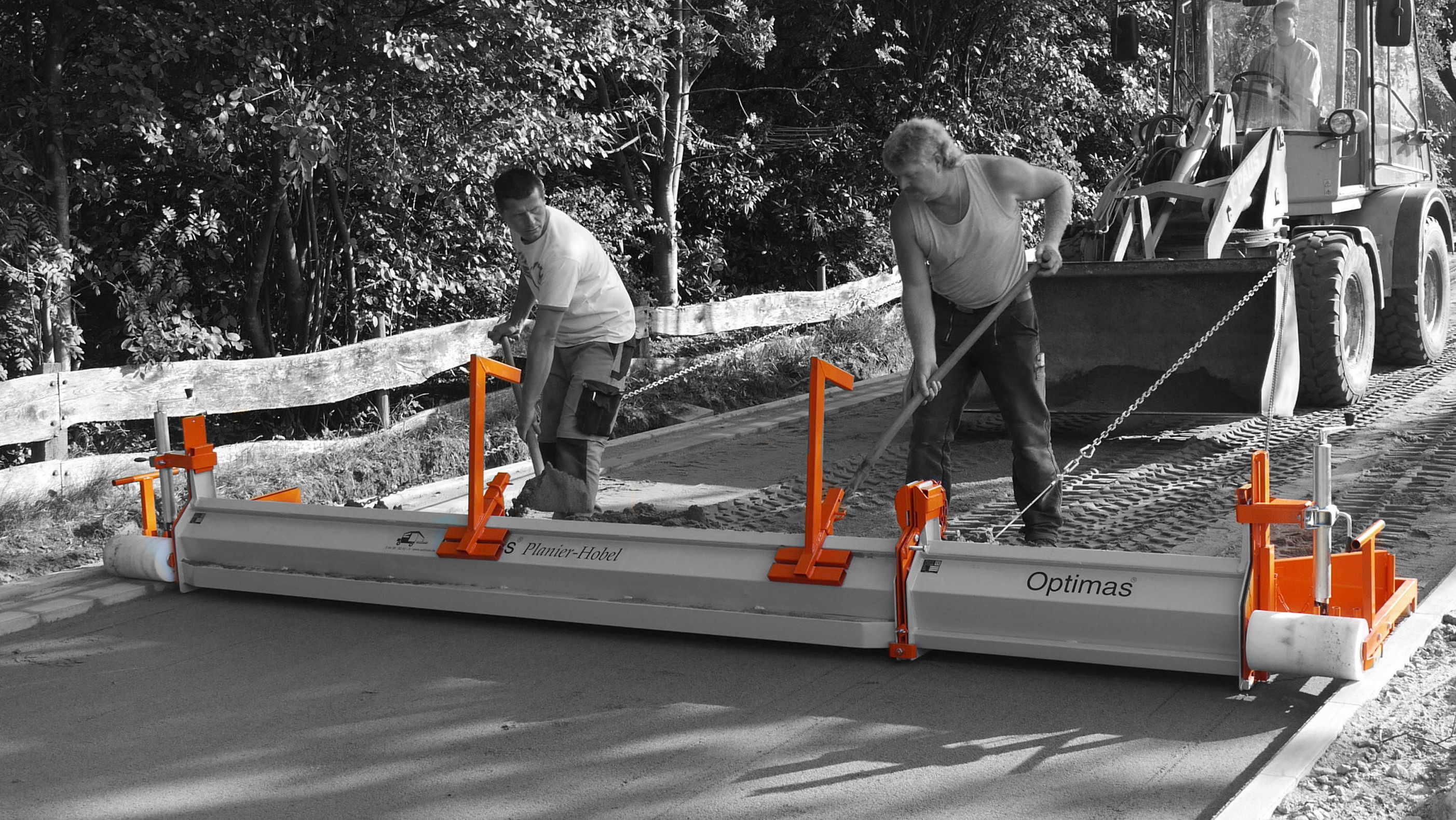 Two workers using a concrete screed machine on a construction site, with a tractor in the background – Optimas.