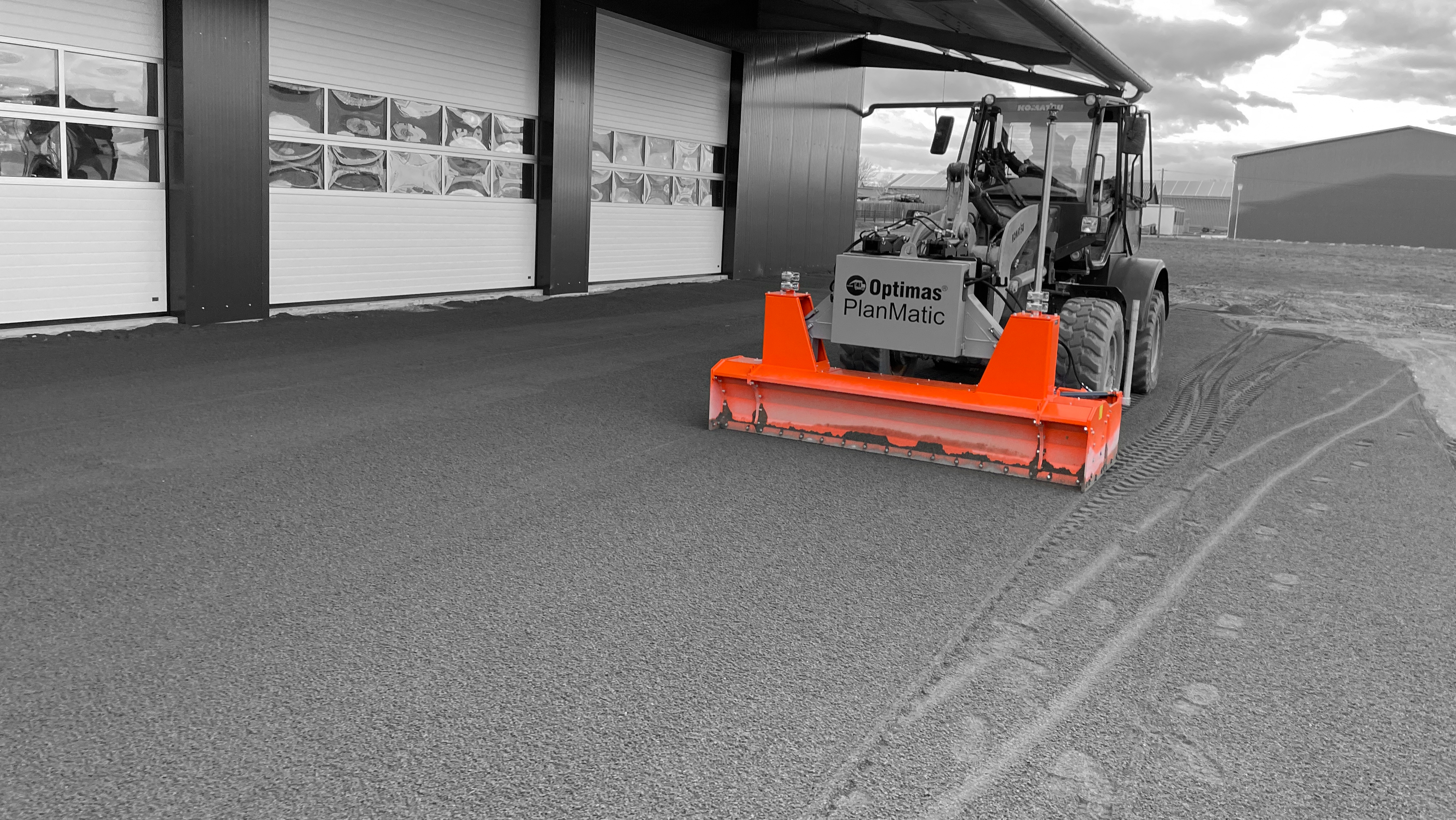 A machine with an orange attachment levels the ground in front of a building, showcasing efficient construction work – Optimas.