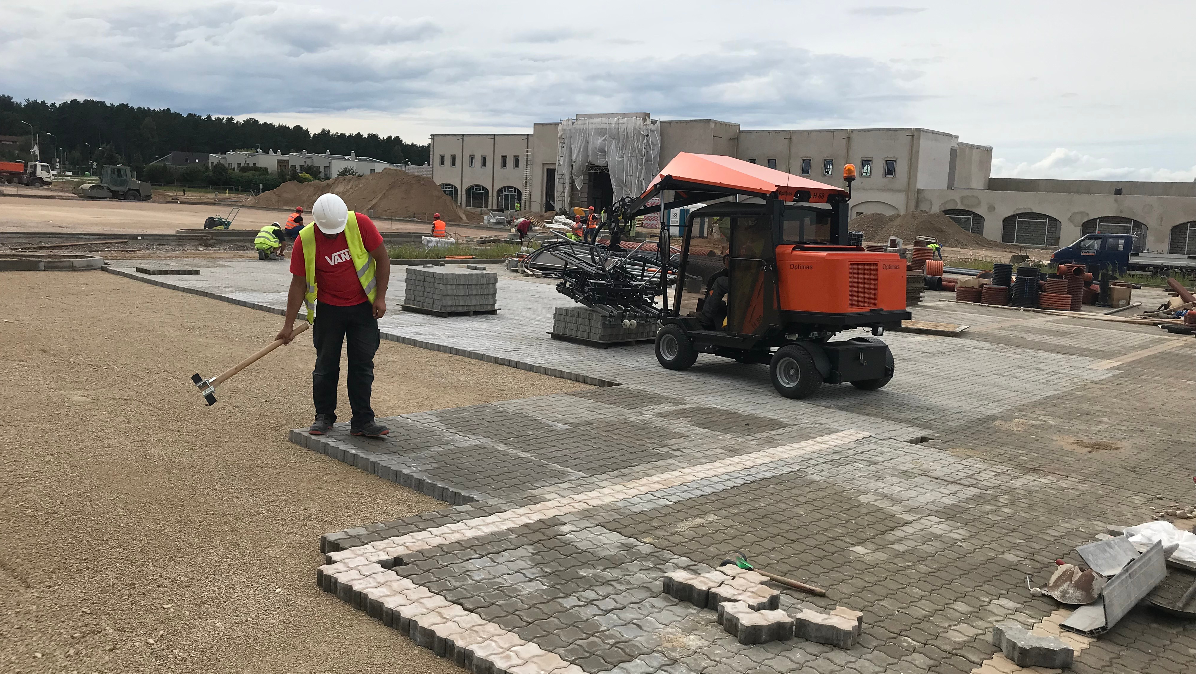 Construction workers laying paving stones with machinery on a building site, showcasing teamwork and equipment use – Optimas.