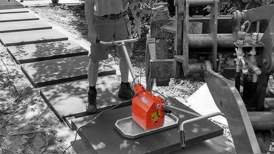 A worker operates a concrete compactor on a construction site with concrete slabs laid out – Optimas.