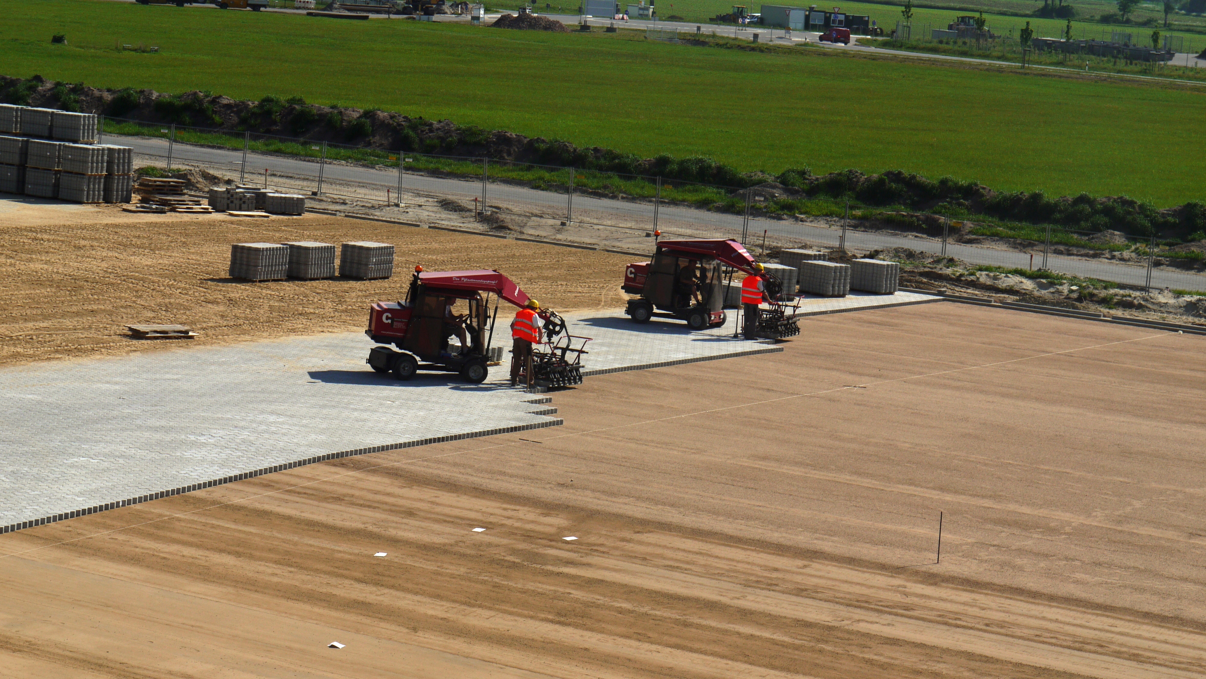Construction site with workers using machinery to lay paving stones on a large area – Optimas.