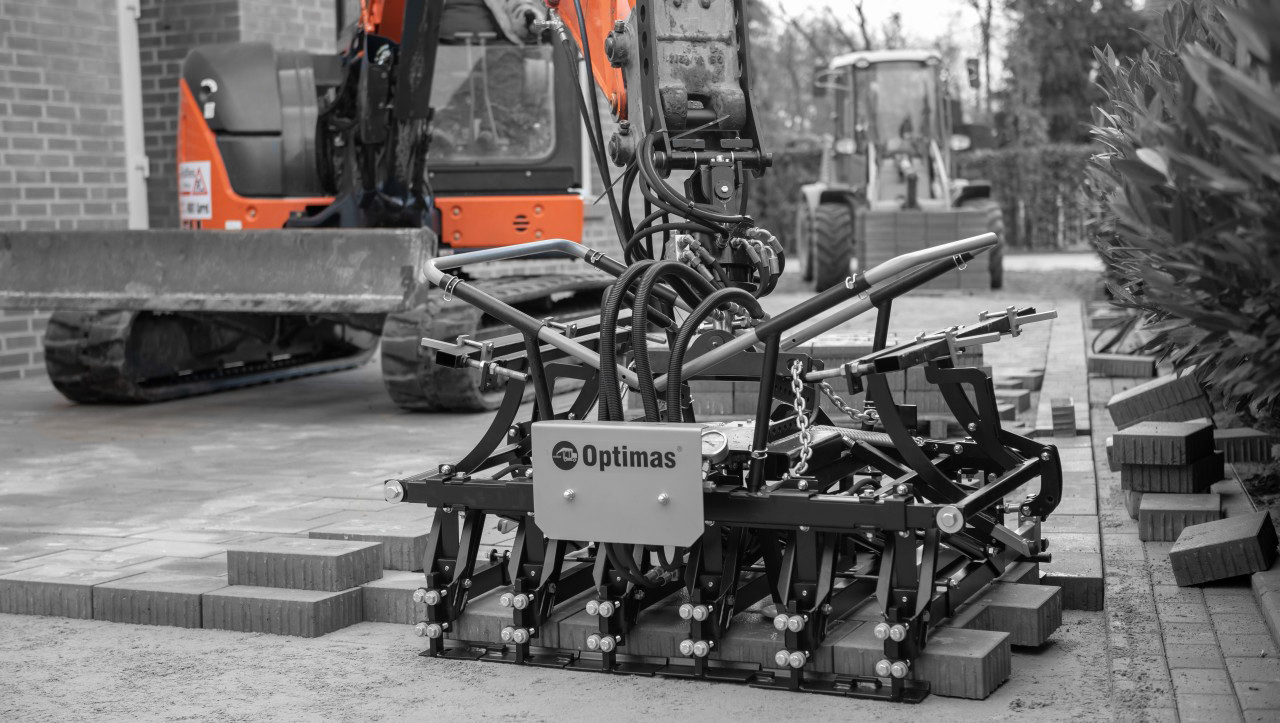 A paving machine with hydraulic components is positioned on a construction site with bricks laid out nearby – Optimas.