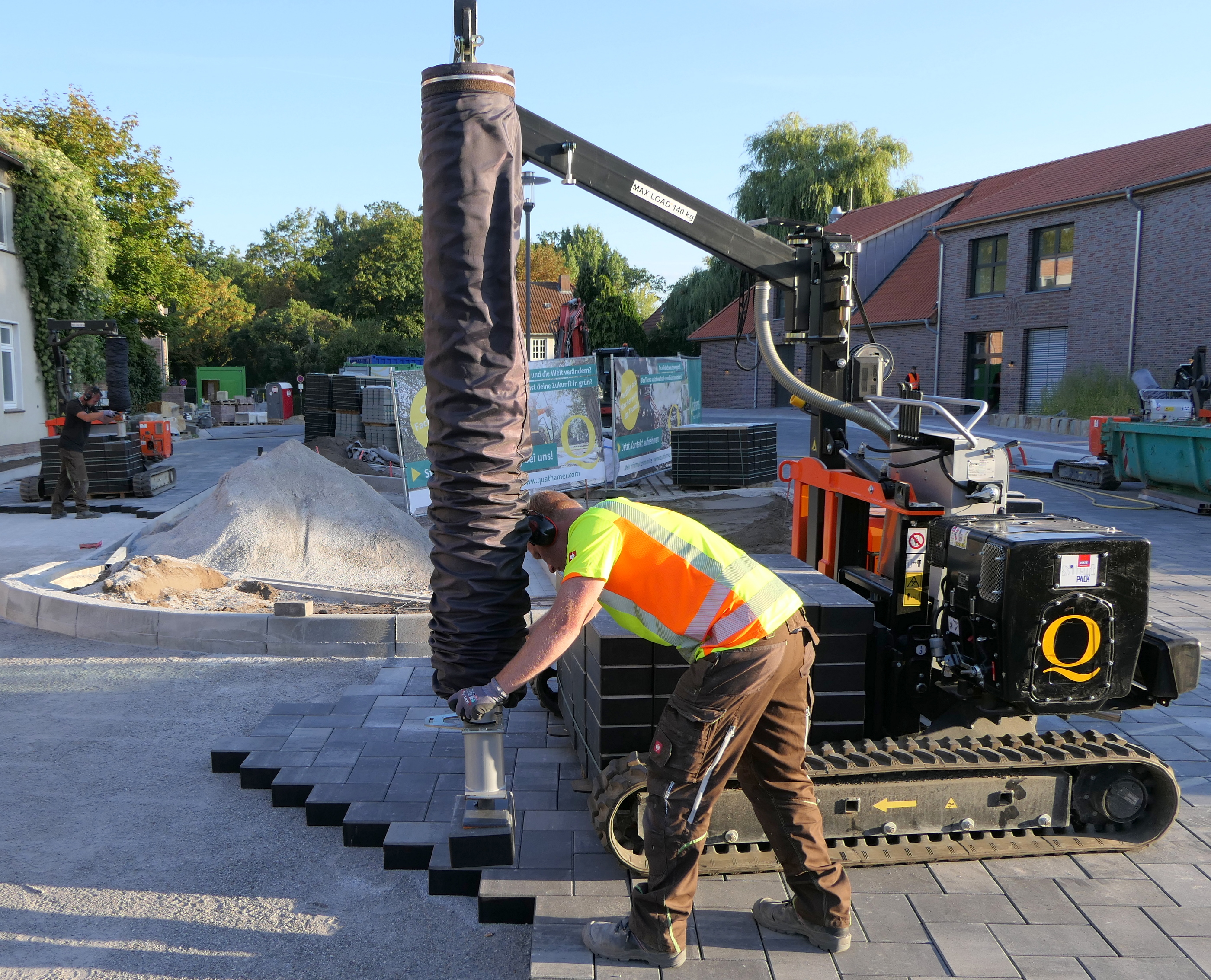 Arbeiter nutzt eine Pflastersteinverlegemaschine auf einer Baustelle, während andere Arbeiter und Materialien anwesend sind, was die Effizienz steigert – Optimas.