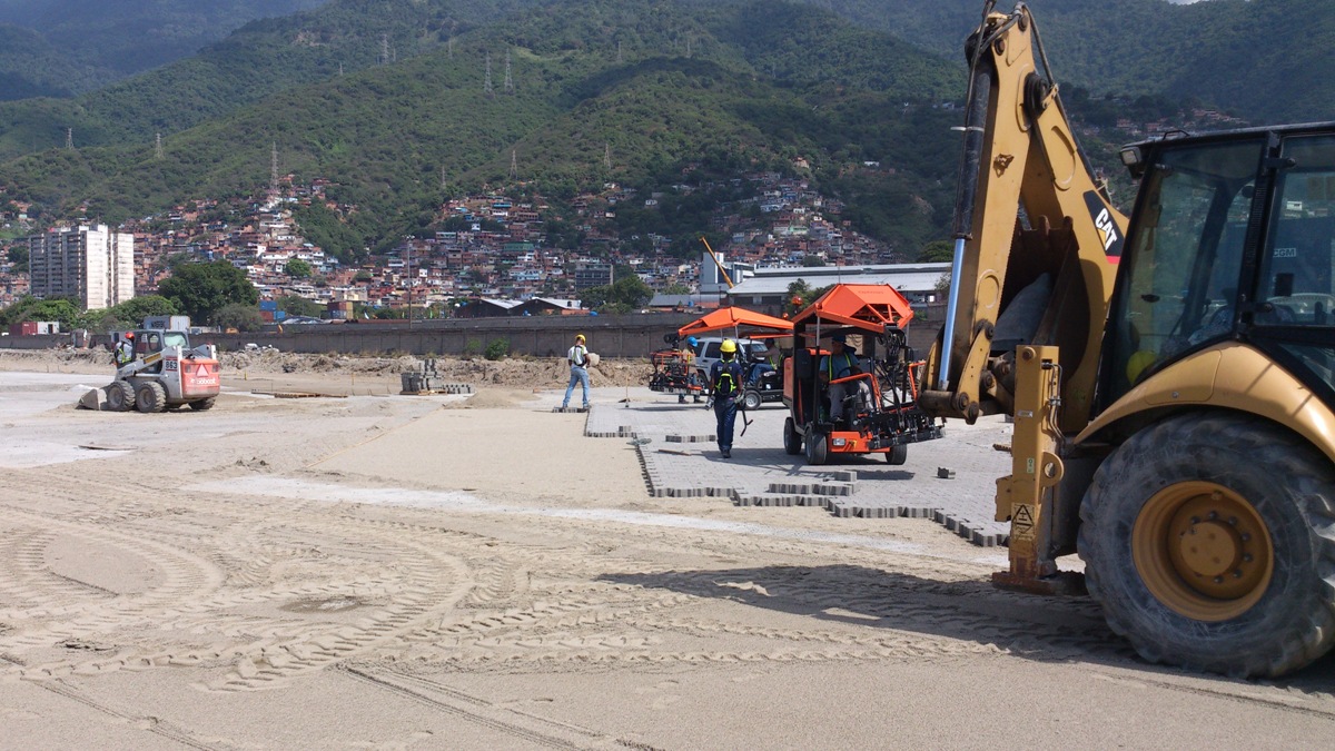 Construction site with heavy machinery and workers laying bricks in a mountainous area – Optimas.
