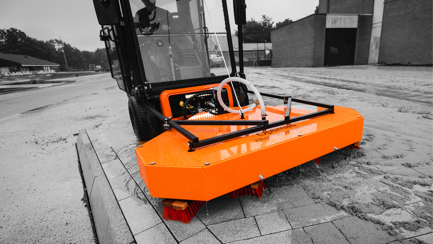 A bright orange street sweeper cleaning a paved area, showcasing its efficient design and functionality – Optimas.