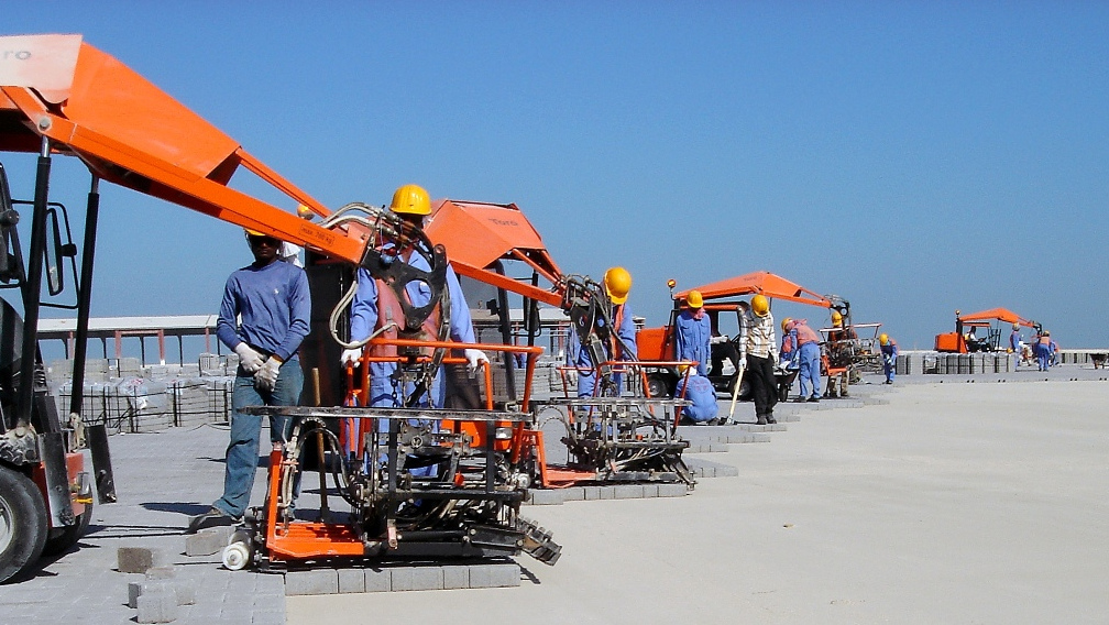 Construction workers using machinery to lay bricks on a sunny day at a construction site – Optimas.