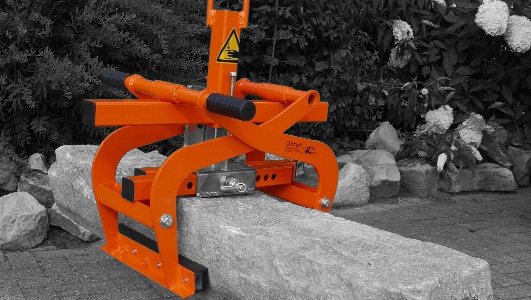 An orange stone lifting tool positioned on a large stone in a garden setting – Optimas.