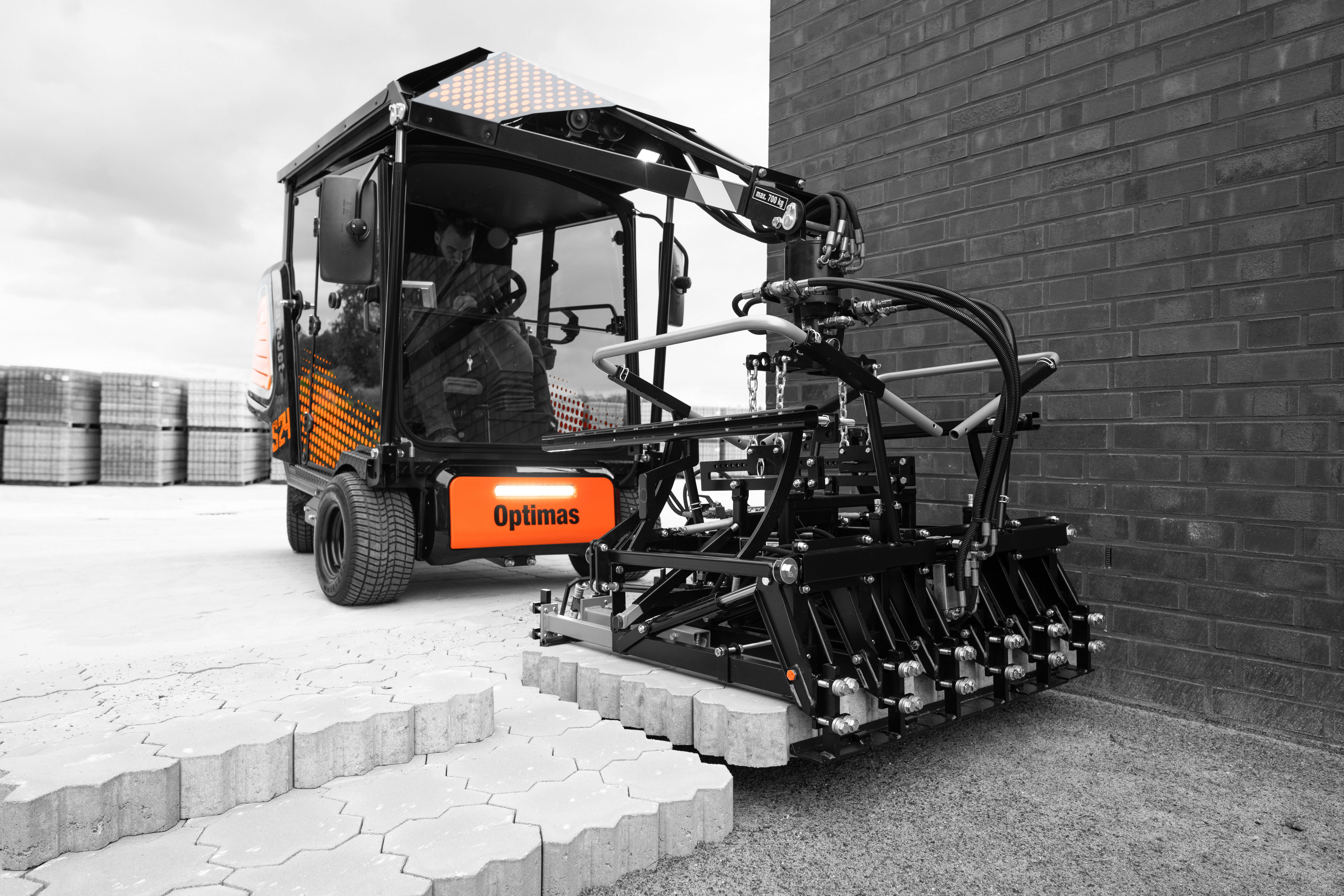 A specialized machine is laying paving stones next to a brick wall, showcasing its operational capabilities – Optimas.