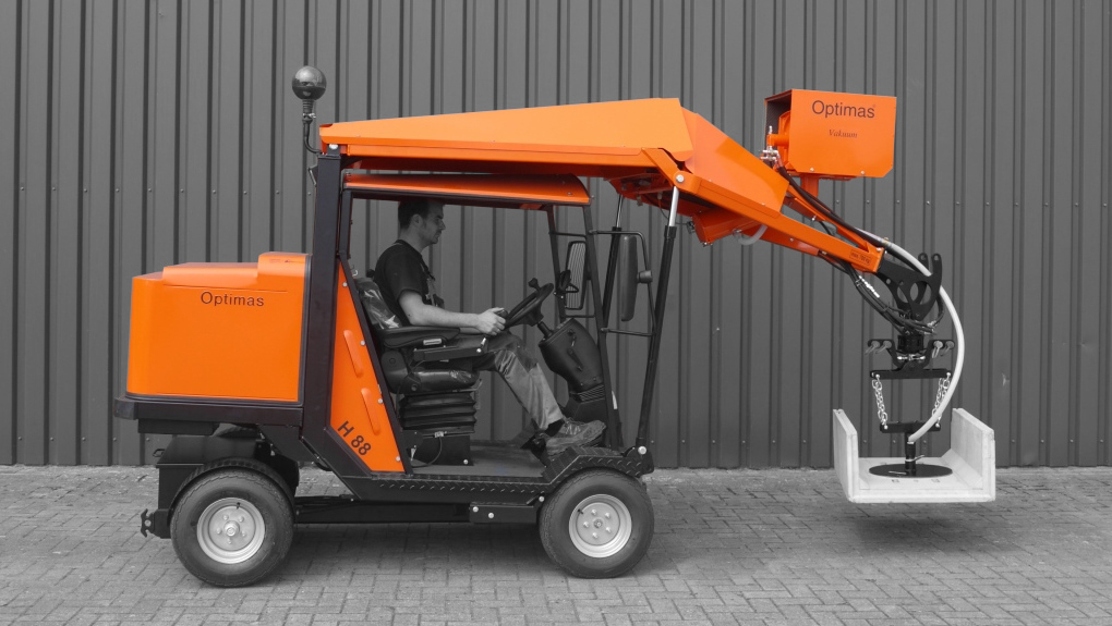 A man operates an orange compact loader with a hydraulic arm and attachment, showcasing its functionality – Optimas.