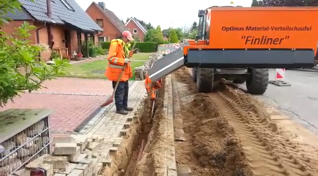 A worker in an orange safety jacket operates a Finliner machine on a construction site, laying materials along a street – Optimas.