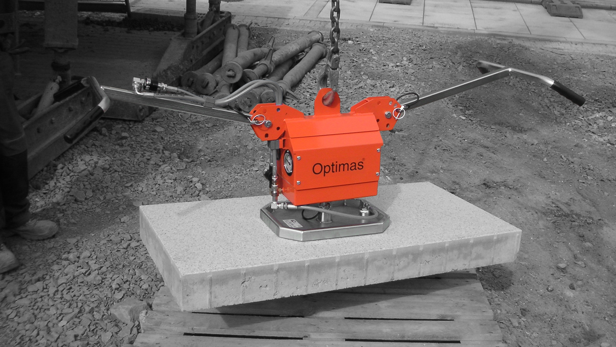 A bright orange lifting device positioned on a concrete slab at a construction site – Optimas.