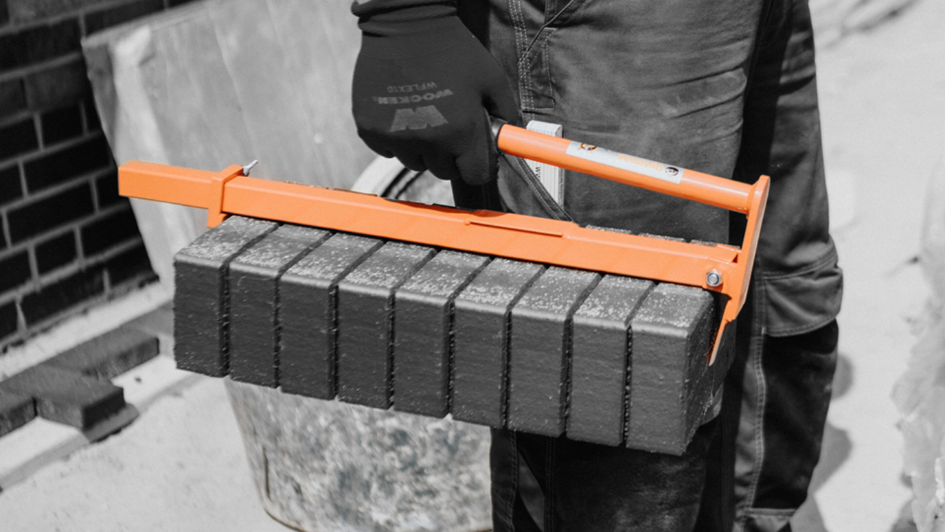 A worker holds a brick carrier tool with several bricks, showcasing construction equipment in use – Optimas.