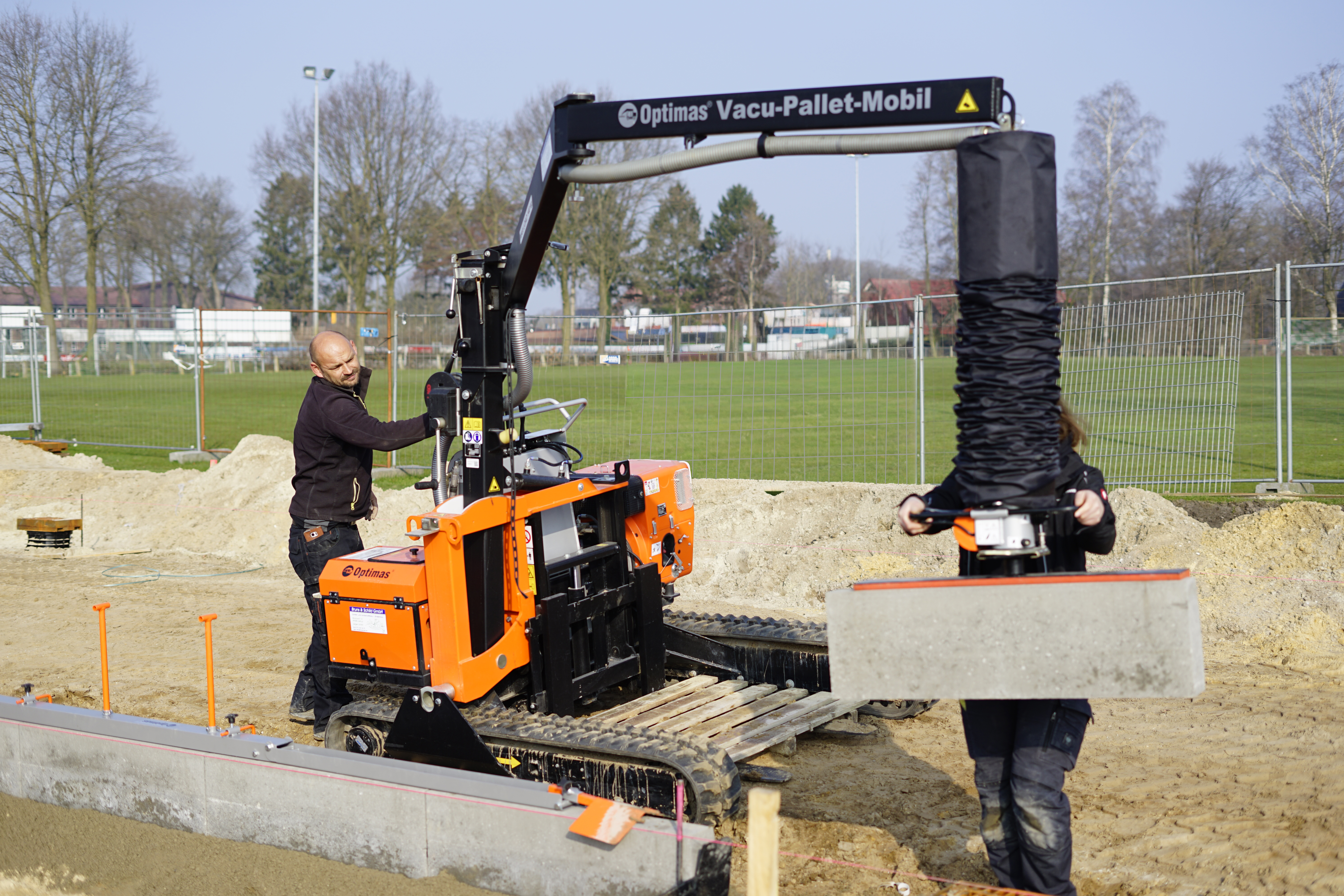 Arbeiter verwenden einen Vakuumheber Optimas Vacu-Pallet-Mobil, um Betonbordsteine ​​auf einer Baustelle zu installieren. Die Arbeiter setzen die Bordsteine ​​präzise – Optimas.