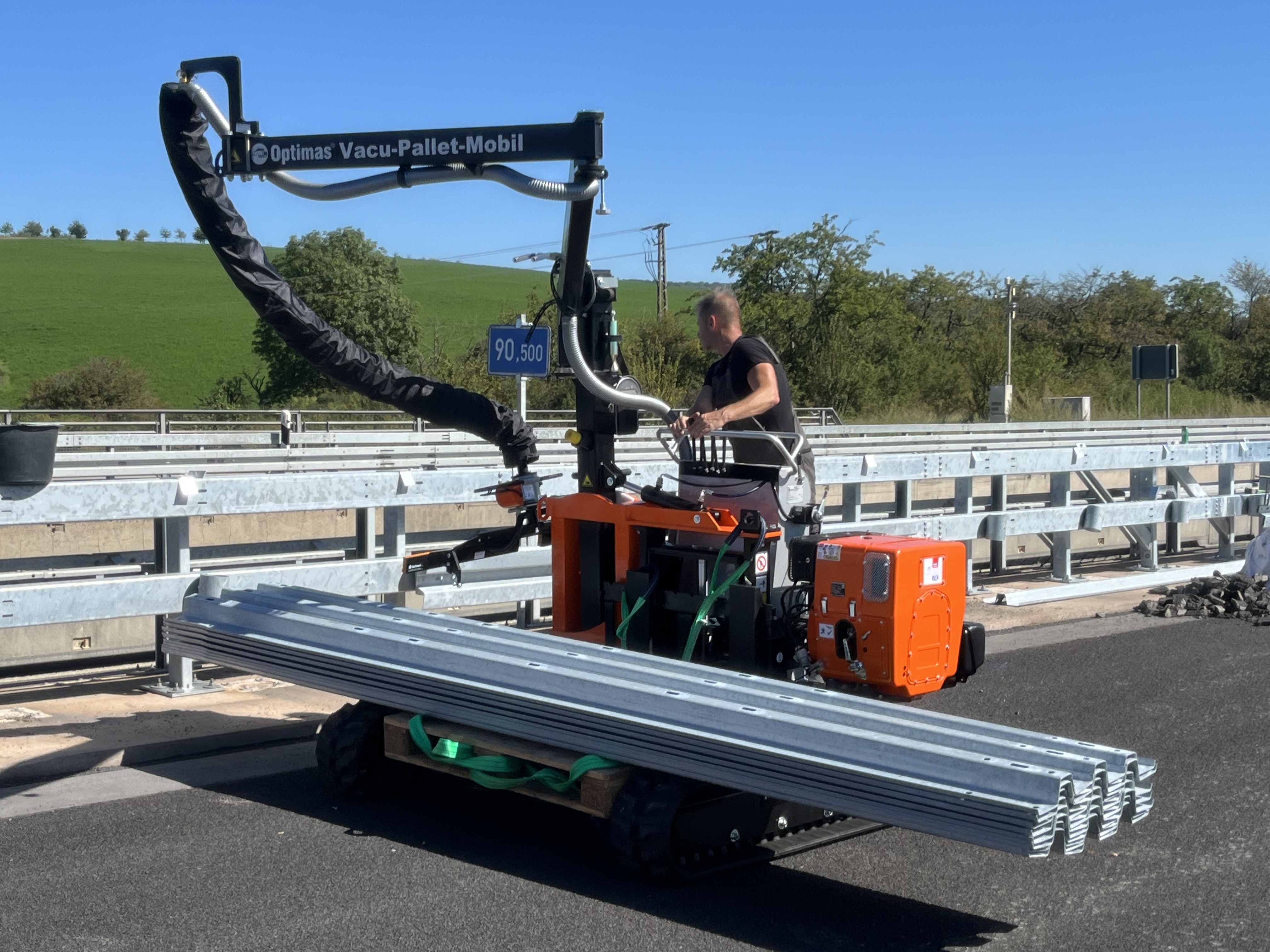 Ein Arbeiter bedient das Optimas Vacu-Paletten-Mobil und hebt Metallträger auf einer Baustelle bei klarem Himmel – Optimas.
