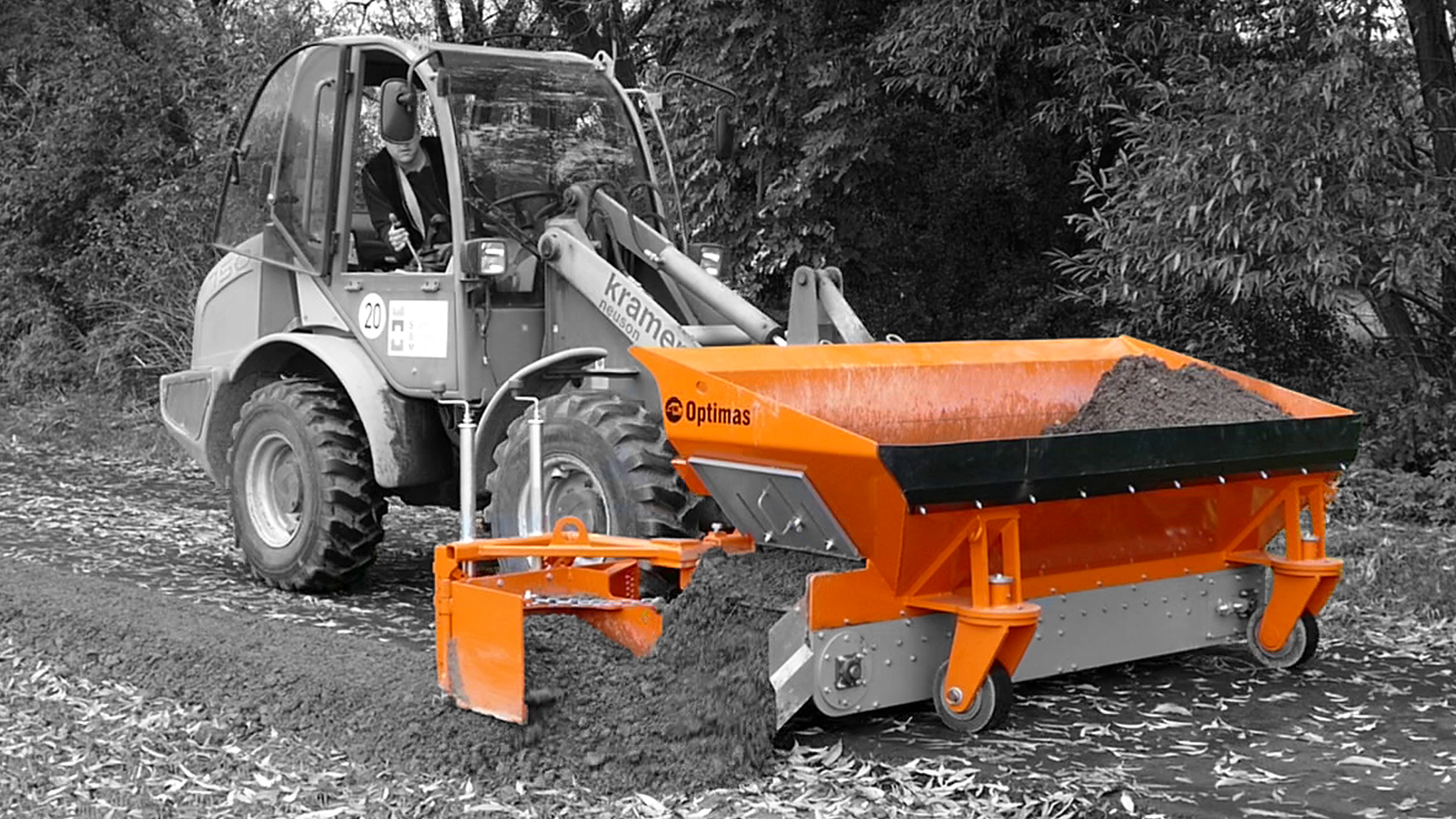 A construction vehicle operates a soil spreader, distributing dirt along a pathway in a natural setting – Optimas.