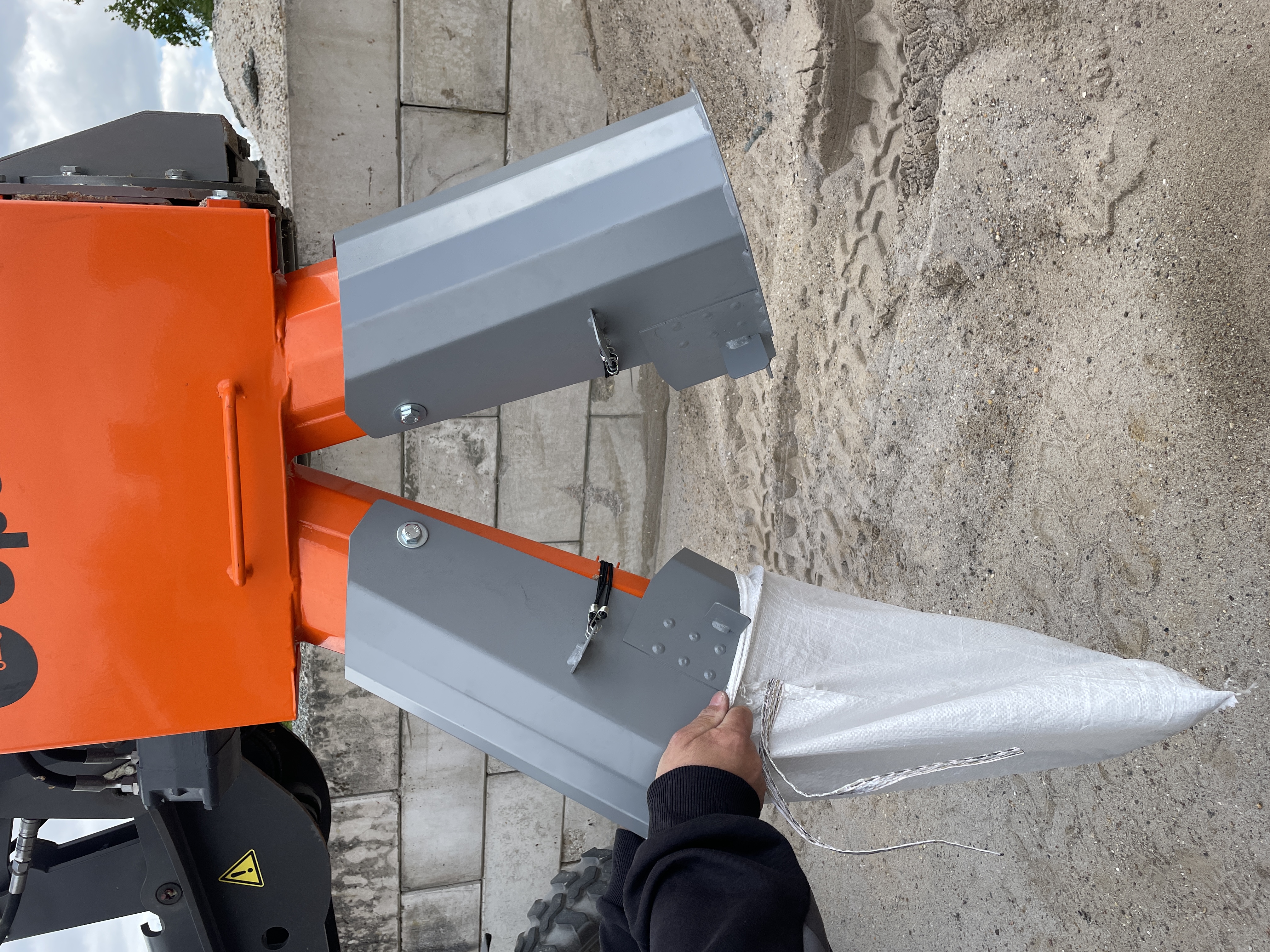 A person holds a white bag while a machine's attachment is positioned above it, ready to dispense material – Optimas.