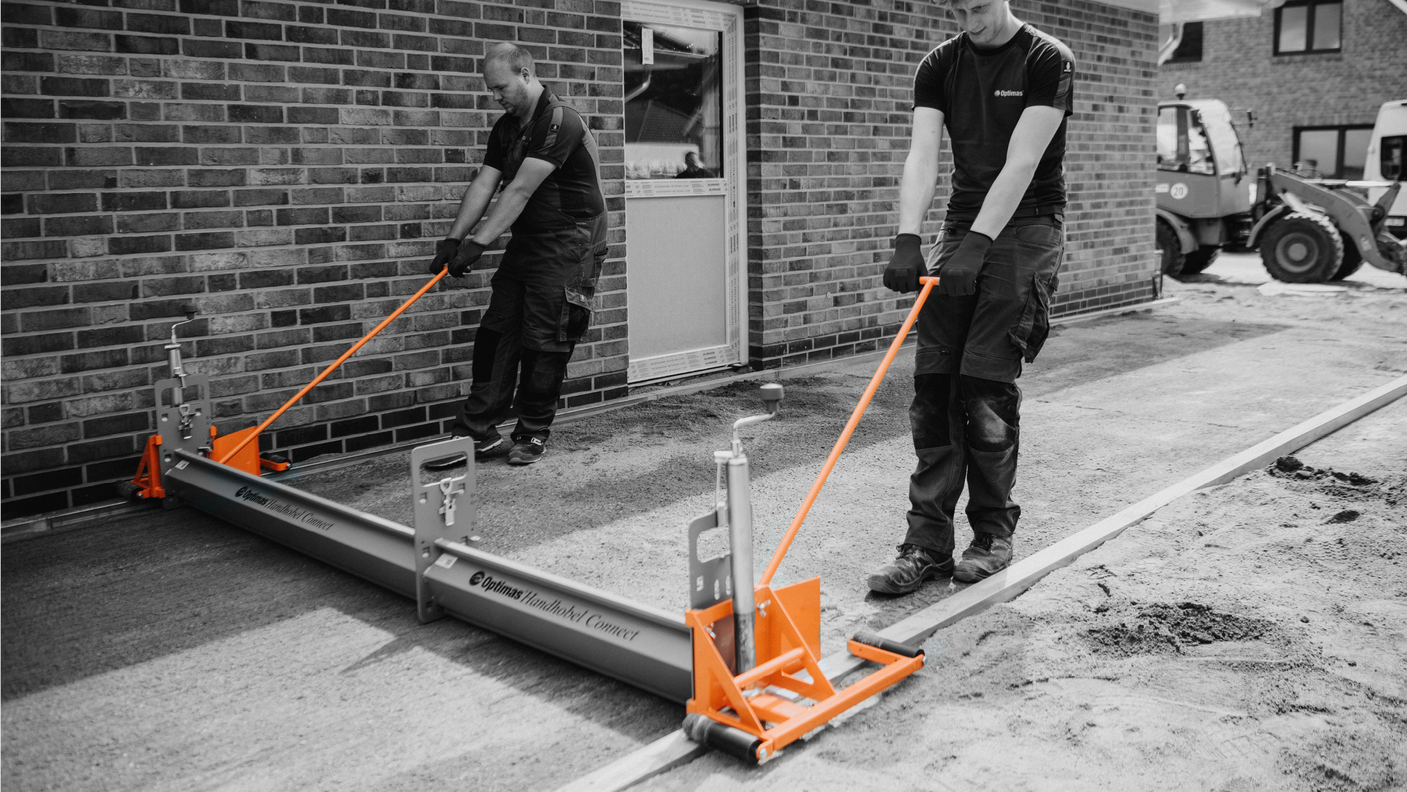 Two workers using a leveling tool to smooth concrete on a construction site – Optimas.