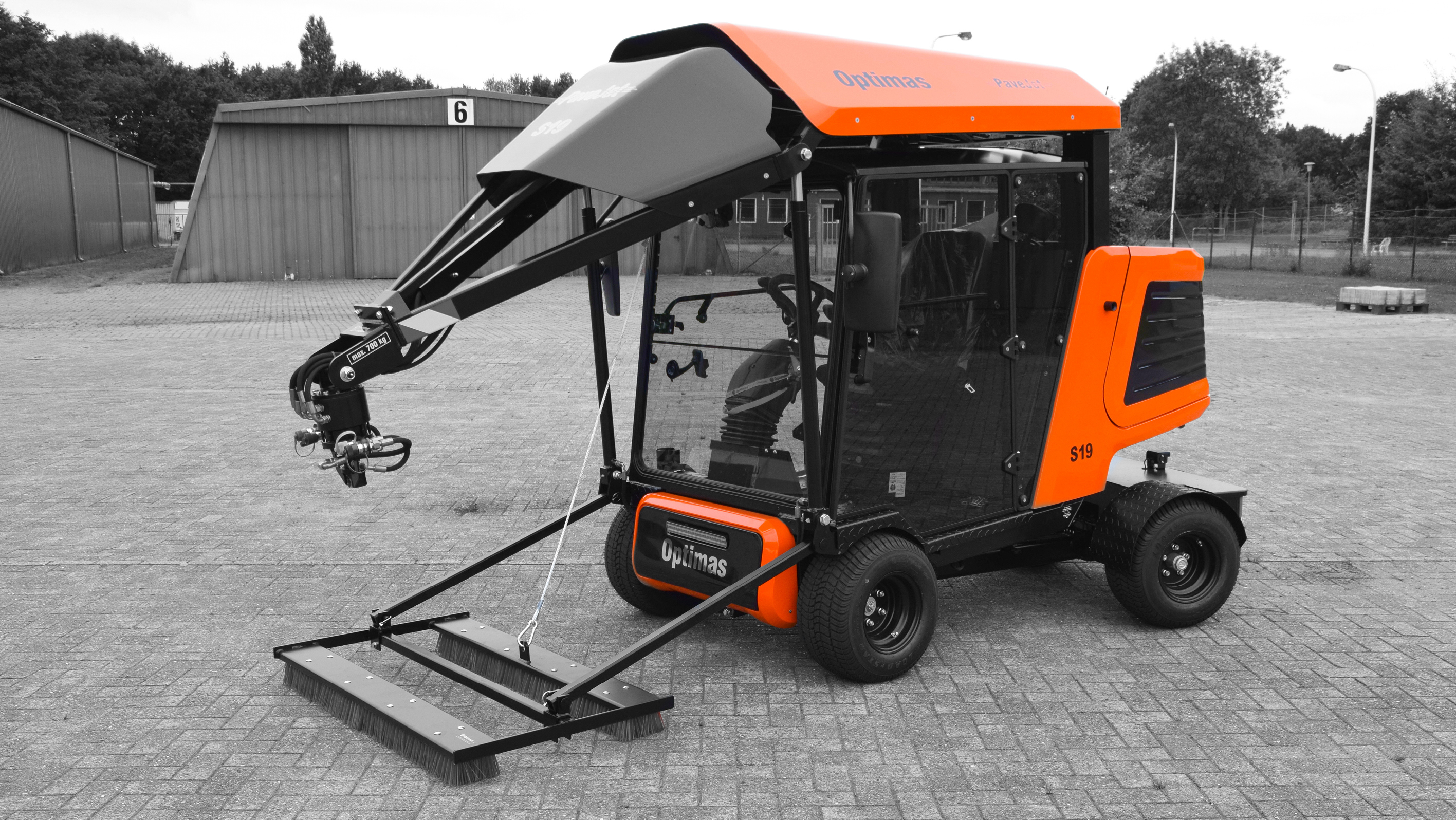 A compact utility vehicle with an orange and black design, featuring a front-mounted brush and articulated arm – Optimas.