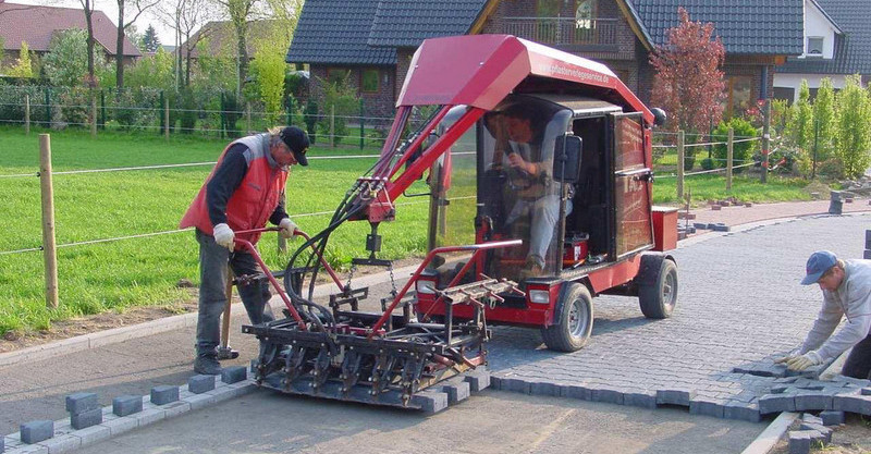 Workers using a paving machine to lay bricks on a driveway in a residential area – Optimas.