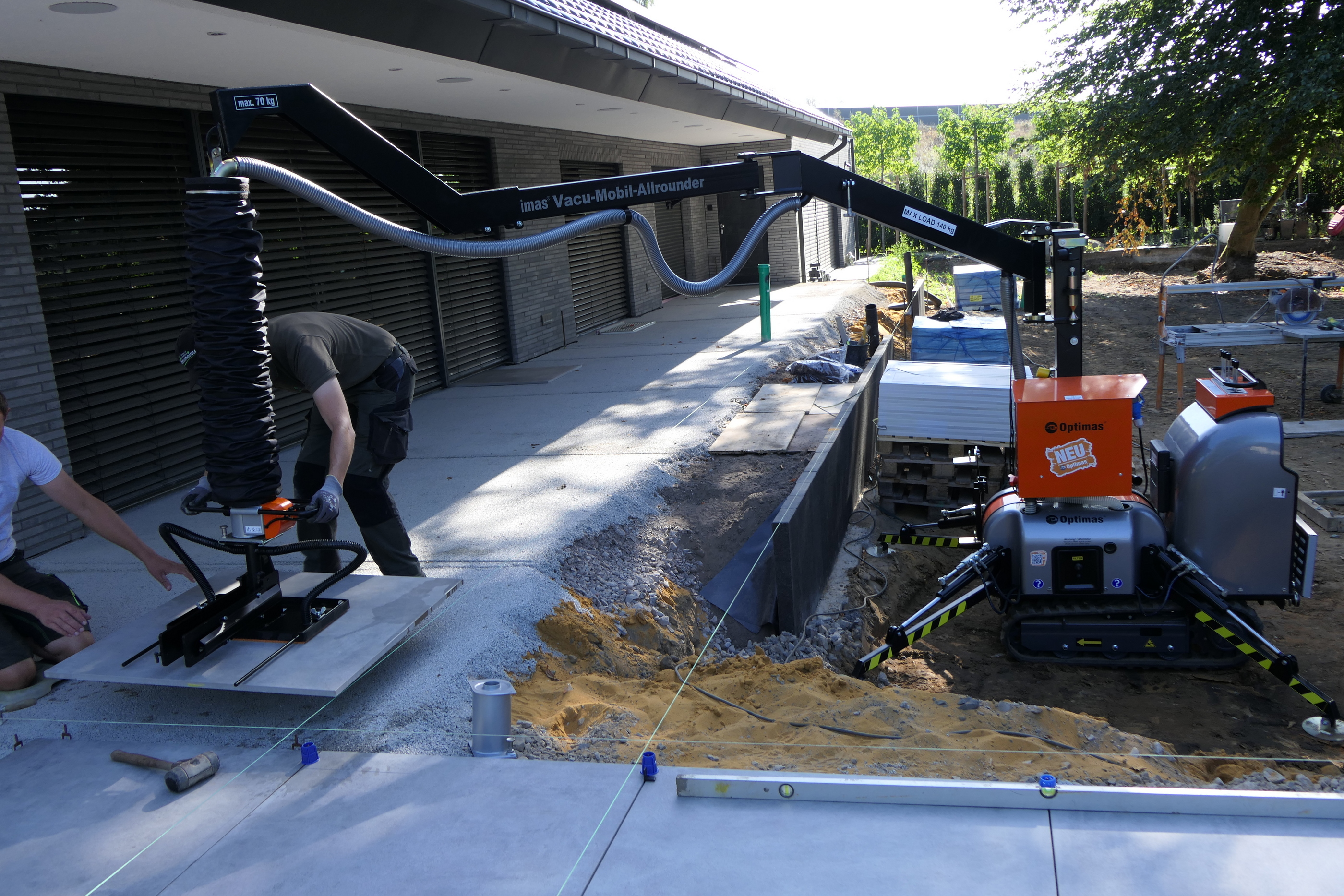 Bauarbeiter heben und verlegen Betonplatten für eine neue Terrasse oder einen Gehweg mit einem Vacu-Mobil-Allrounder von Optimas – Optimas