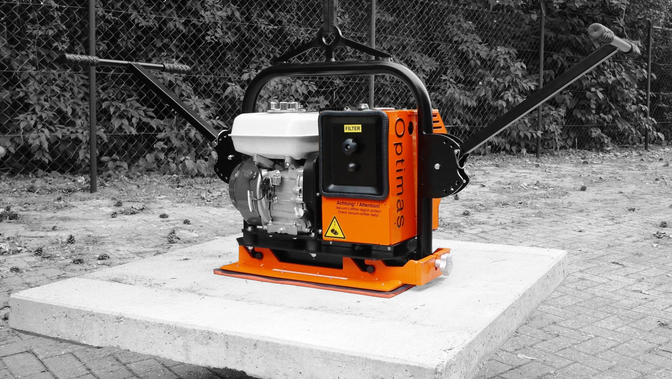 A compact, orange and black vibrating plate compactor on a concrete base, designed for efficient soil compaction – Optimas.