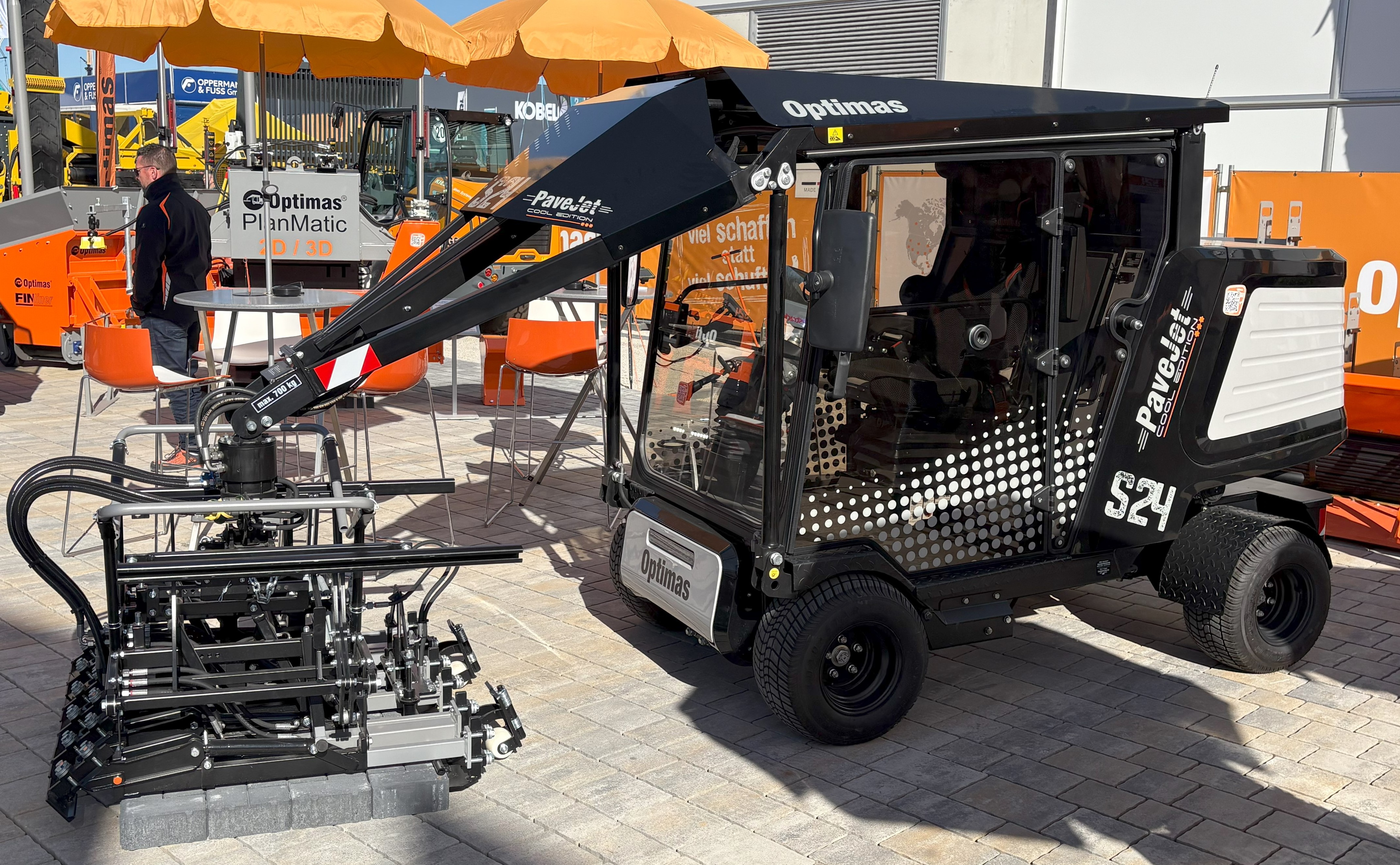 Der Optimas PaveJet S24, ein Cool-Edition-Fertiger, wird mit seinem über ausgestellte Pflastersteine ​​ausgestreckten Roboterarm präsentiert, der für Effizienz sorgt – Optimas.