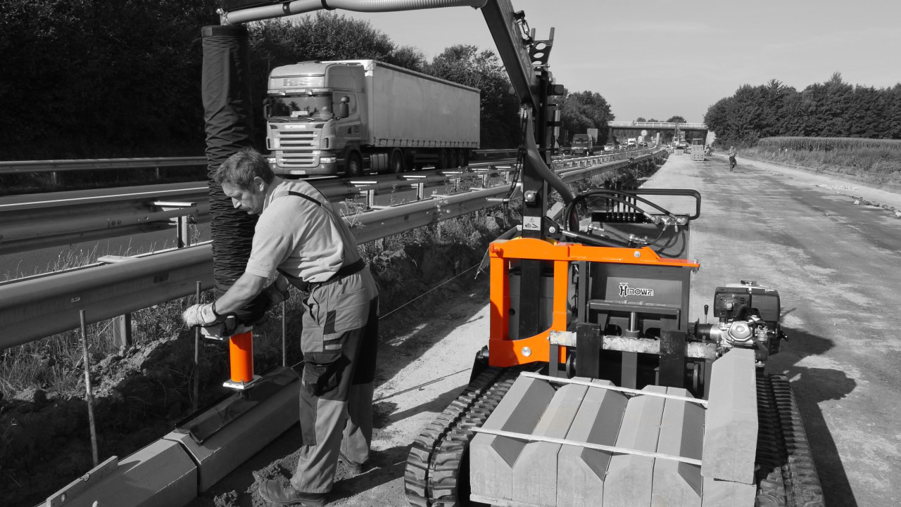 A worker operates a construction machine on a highway, with trucks passing in the background – Optimas.