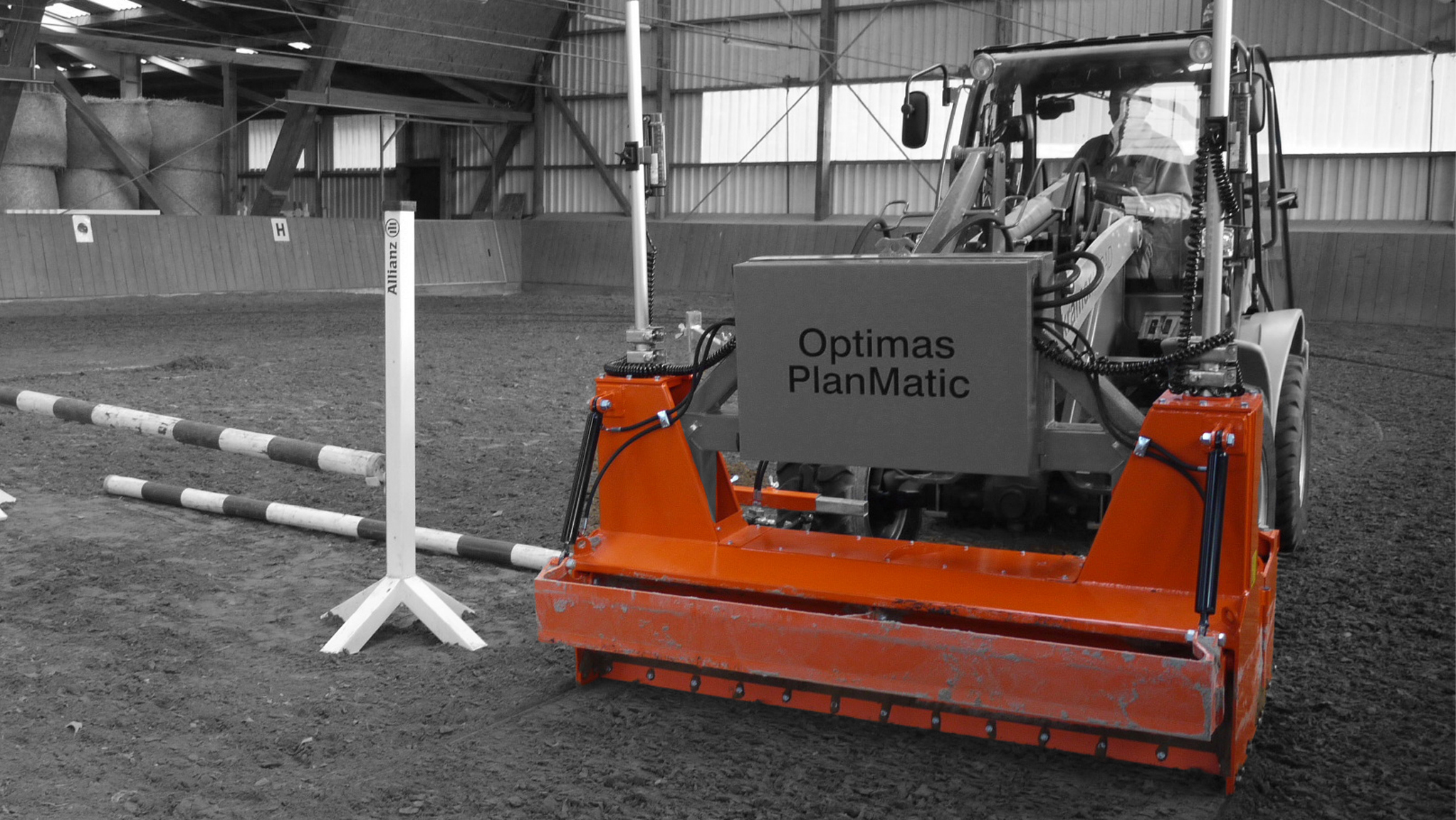 An orange agricultural machine with a box labeled 'Optimas PlanMatic' in a riding arena setting – Optimas.
