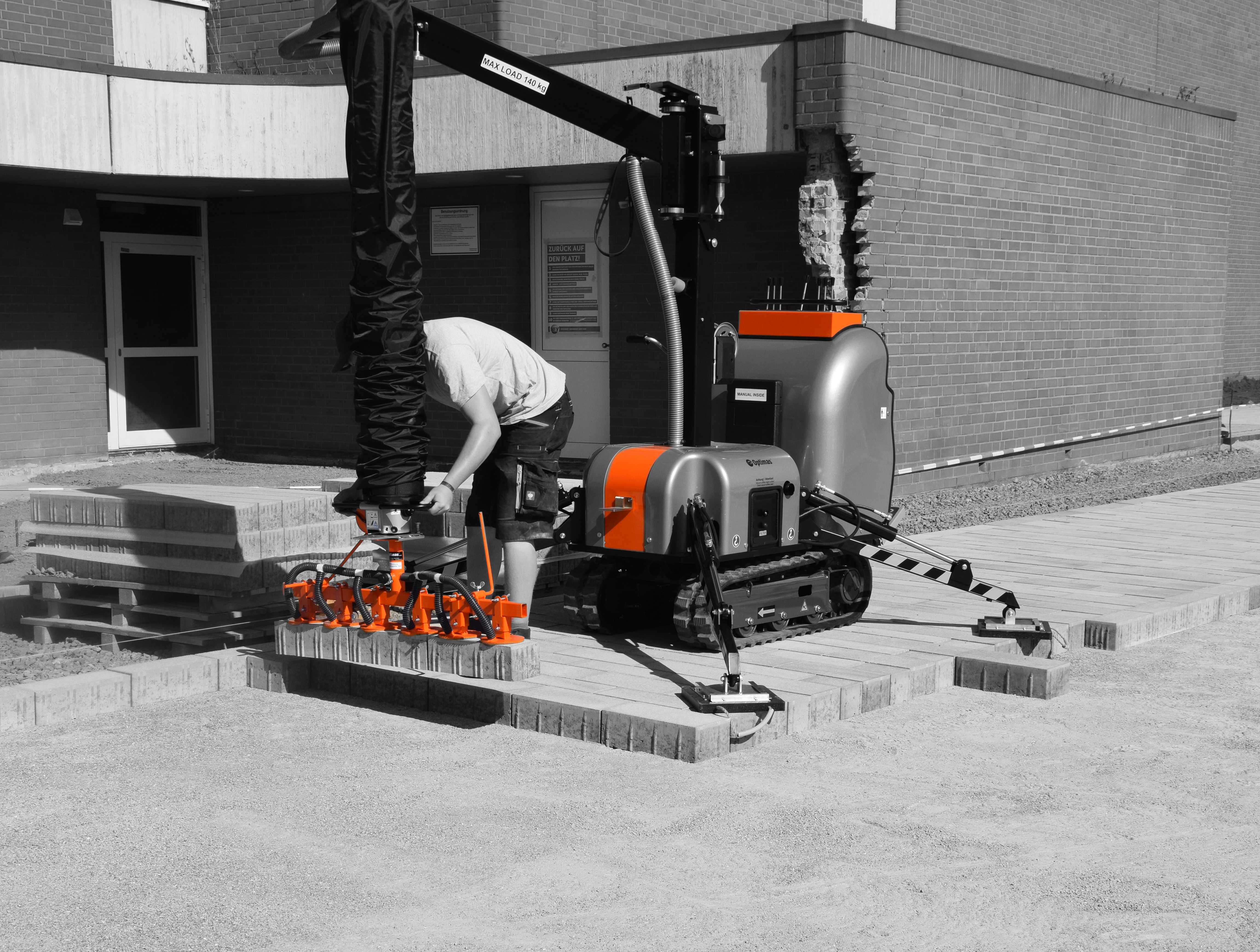 A worker operates a compact construction machine laying bricks on a pathway at a construction site – Optimas.