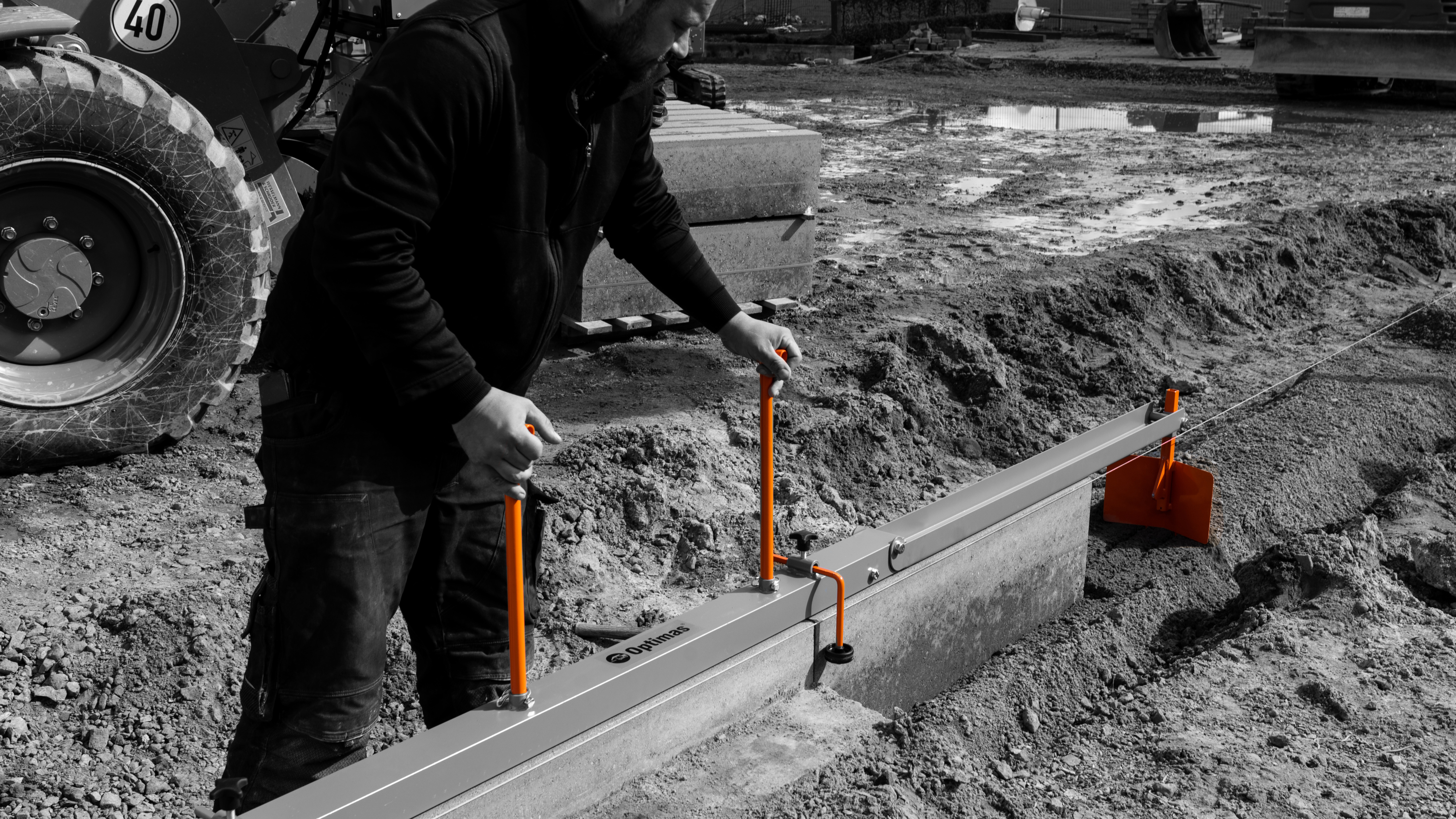 A construction worker using a leveling tool on a job site with machinery in the background – Optimas.