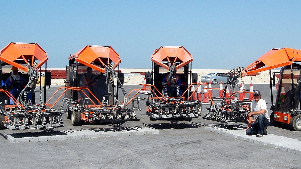 A construction site featuring multiple Toro machines and a worker preparing for paving tasks – Optimas.