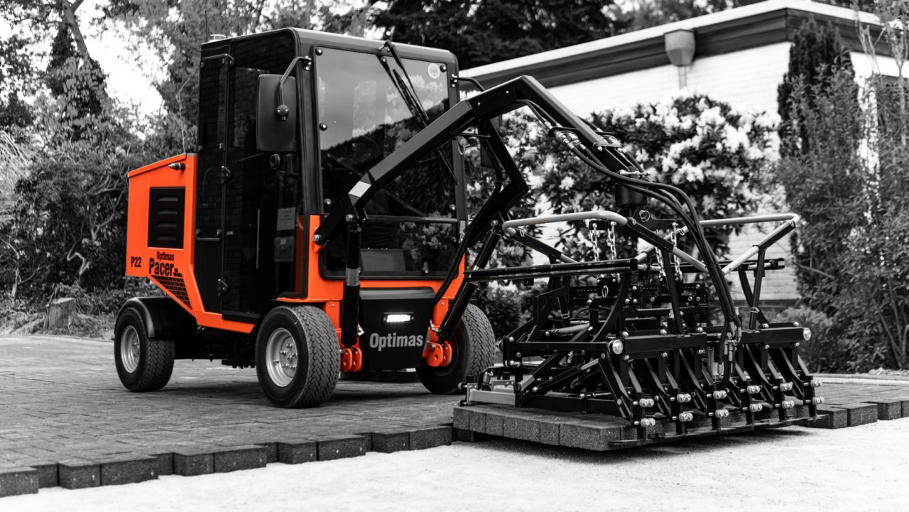 A compact construction machine with an orange and black design, equipped for paving work – Optimas.