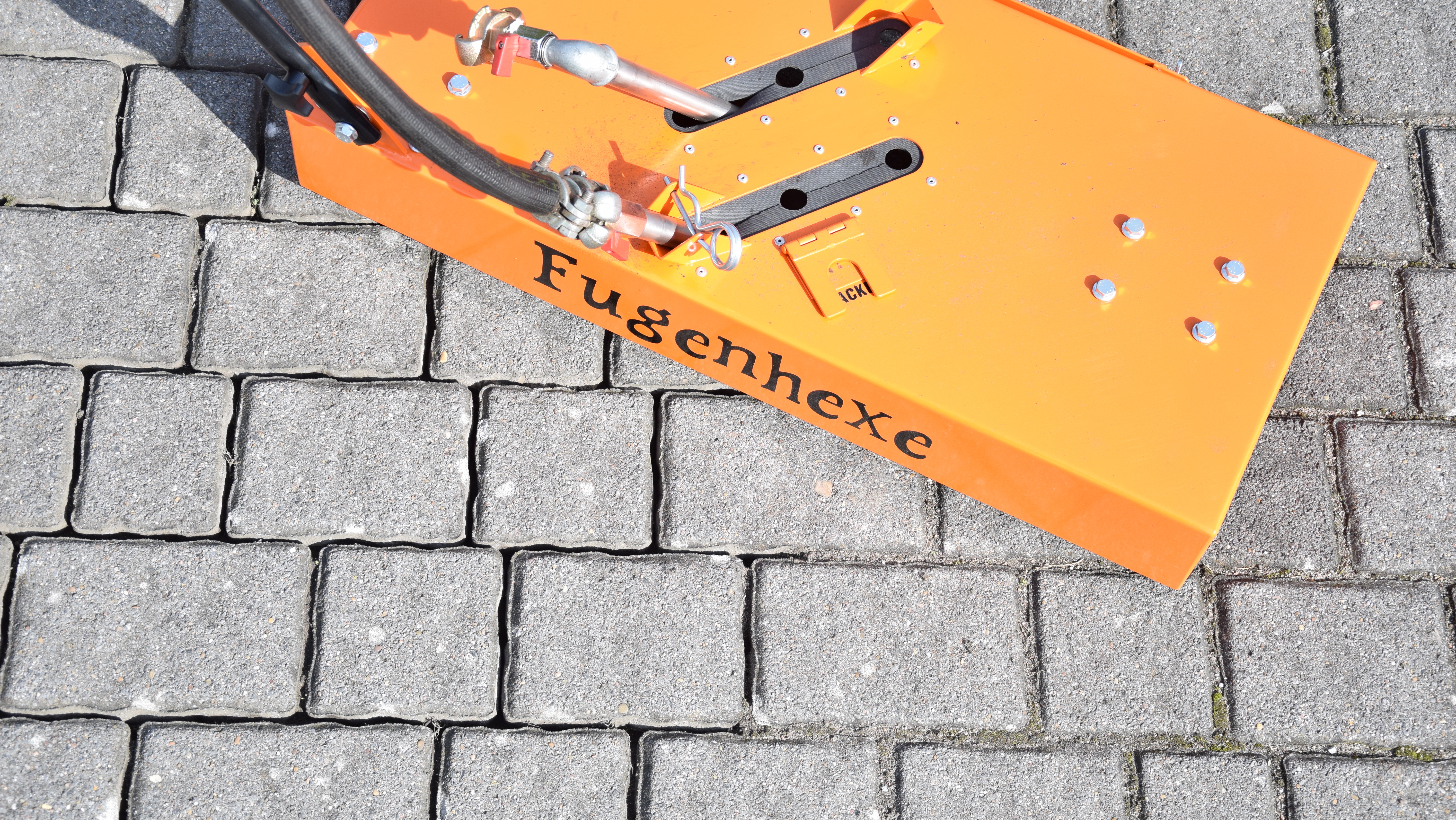 An orange paving machine attachment labeled 'Fugenhexe' on a stone pavement surface – Optimas.